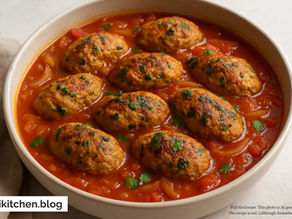 Bowl of golden-brown veggie patties in vibrant red tomato sauce. Text: aikitchen.blog. Warm, inviting ambiance.