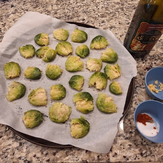 parchment paper lined tray with Smashed sprouts, next to it, bottle of olive oil, minced garlic and a bowl with spices