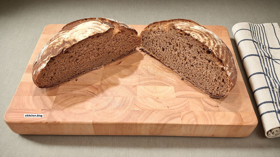 Two halves of rustic bread on a wooden board, with a striped cloth beside. The board has a small label: aikitchen.blog. Warm tones.