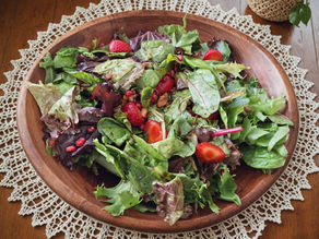 A vibrant salad in a wooden bowl with mixed greens, strawberries, and pomegranate seeds on a lace tablecloth, evoking a fresh, healthy mood.