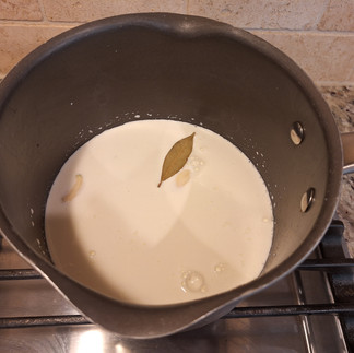 In a saucepan, heat the milk and cream with the garlic and bay leaf. Let it steep on low for about 10 minutes, then strain. In another saucepan, melt butter over medium heat. Whisk in flour and cook for 1-2 minutes. Gradually whisk in the warm milk mixture, continuing to cook and whisk until thickened (about 5-7 minutes). Add nutmeg, salt, and pepper to taste.