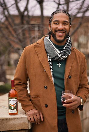 Pictured: Justin Fox in a brown jacket and checkered scarf outside in the Fall