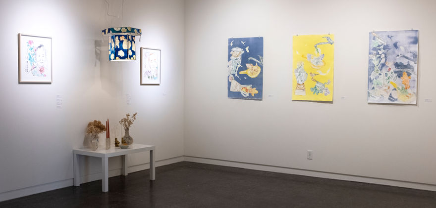 Blue and white cylinder light hangs from the ceiling. Small white rectangular table under the light. Small rectangular painting on white canvas with older face.