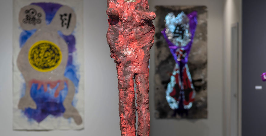 photo of gallery with large red sculpture with legs and paintings in background 