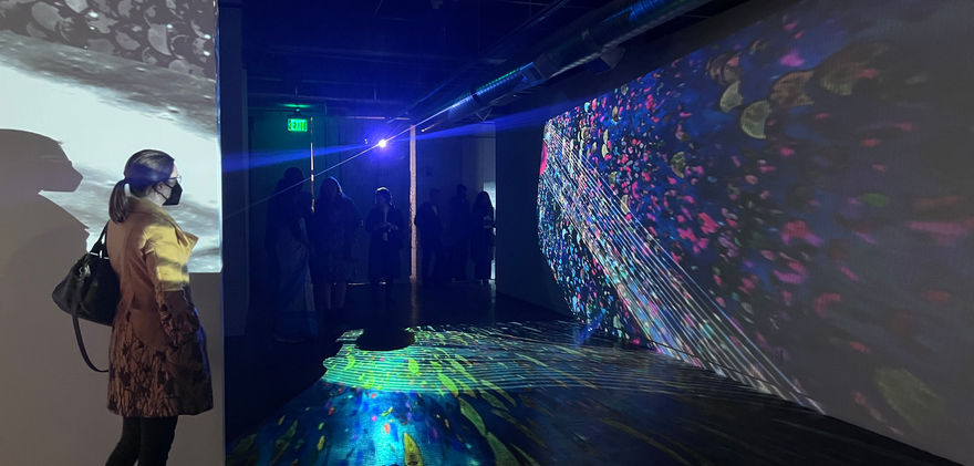 Woman stands against wall and looks at colorful space imagery projected on wall.