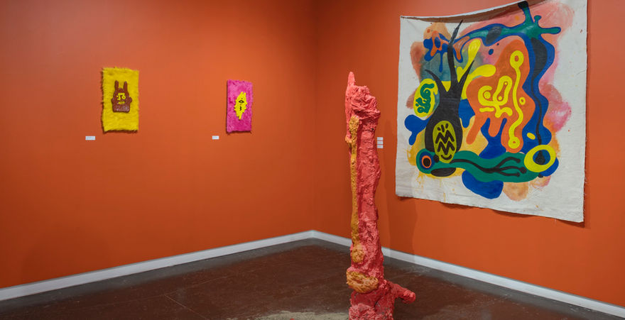 gallery space with orange walls and three abstract paintings with abstract sculptural form