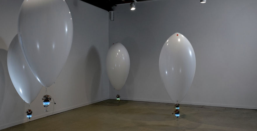 gallery with large white balloon forms at eye level with blue lights hanging from them