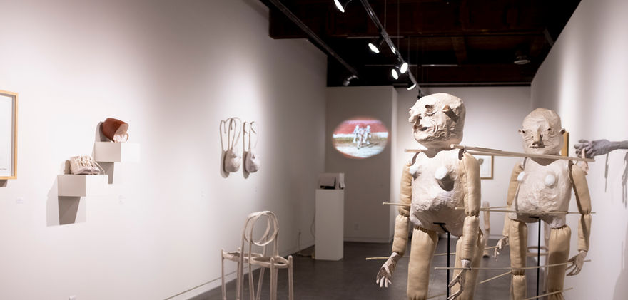 Wide exhibition shot, paper-made figures and objects in the room, on the wall and free-standing.