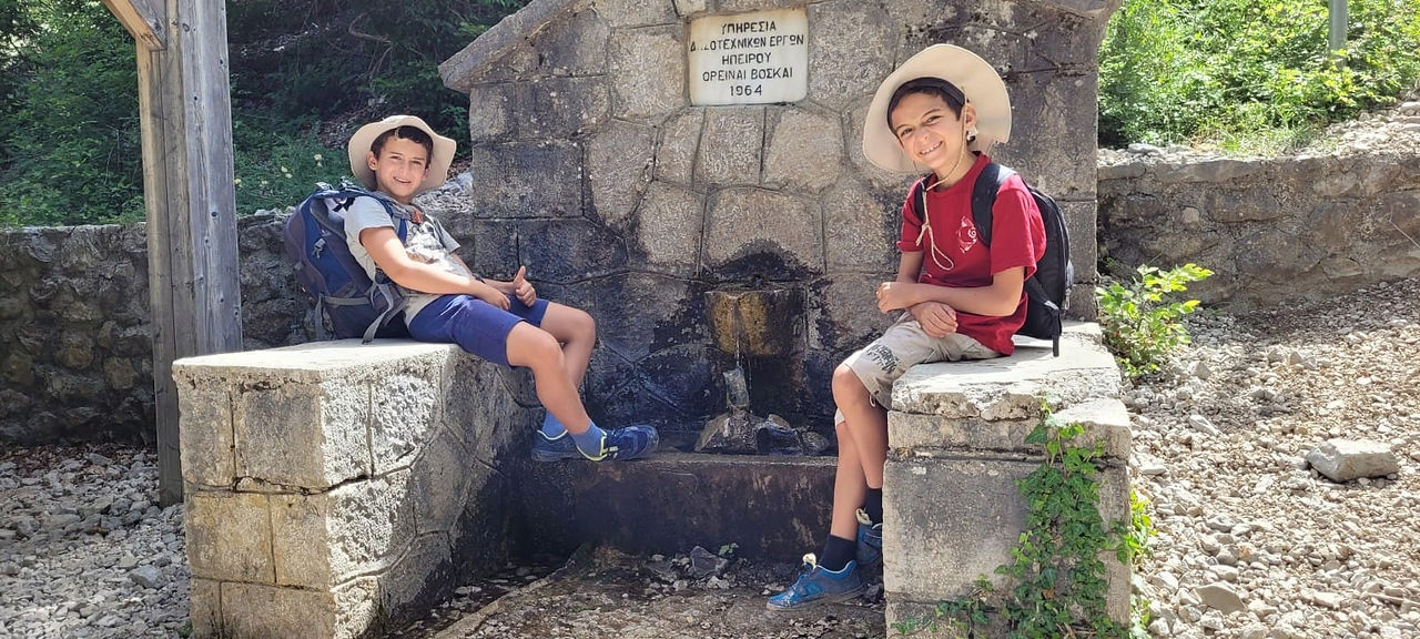 שני מטיילים צעירים יושבים ליד מזרקת אבן בזגוריה