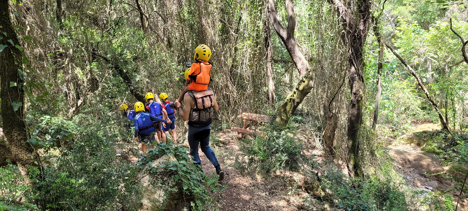 ילד על כתפי מבוגר עם קסדה וחגורת הצלה ביער