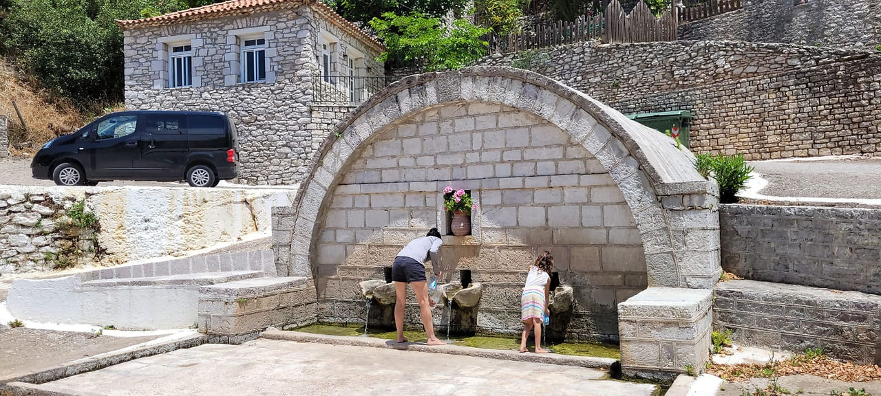 אישה וילדה שואבות מים ממזרקת אבן בכפר