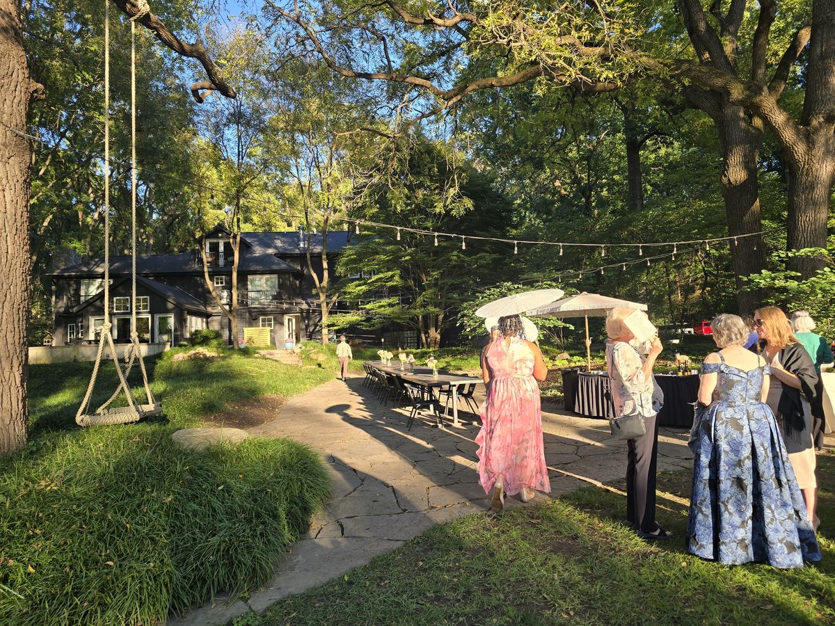 Wedding guests gather outside among the trees in the late-afternoon sunshine.