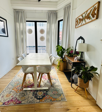 An office with a table and four white chairs a side table with plants and wall art