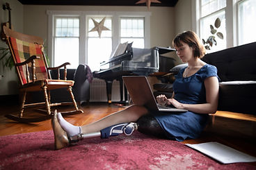 A woman with a prosthetic sitting on the floor while looking at her laptop in her home