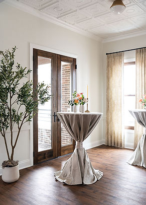 Event room with cocktail table, plant, and wooden doors.
