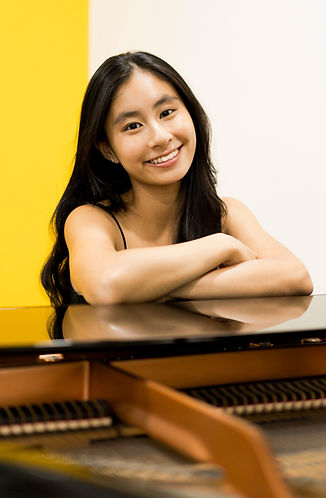asian long haired female with hands crossed on top of a grand piano