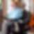 Claire is a white woman, of about 25-30 years old. She wears glasses and has long brown hair, which is tied back in this photo. She is a wheelchair user, and is sitting in her powerchair. She is wearing a blue jumper and grey jeans. She has an orange backpack on her wheelchair. She is smiling at the camera which is faced to her right.