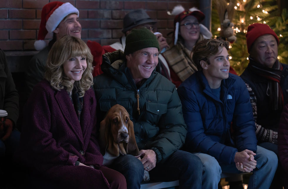 Smiling crowd in winter coats and Santa hats sits by a brick wall, with a basset hound and glowing Christmas lights behind them