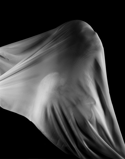 Black and white studio portrait of a person with white flowing fabric over their face
