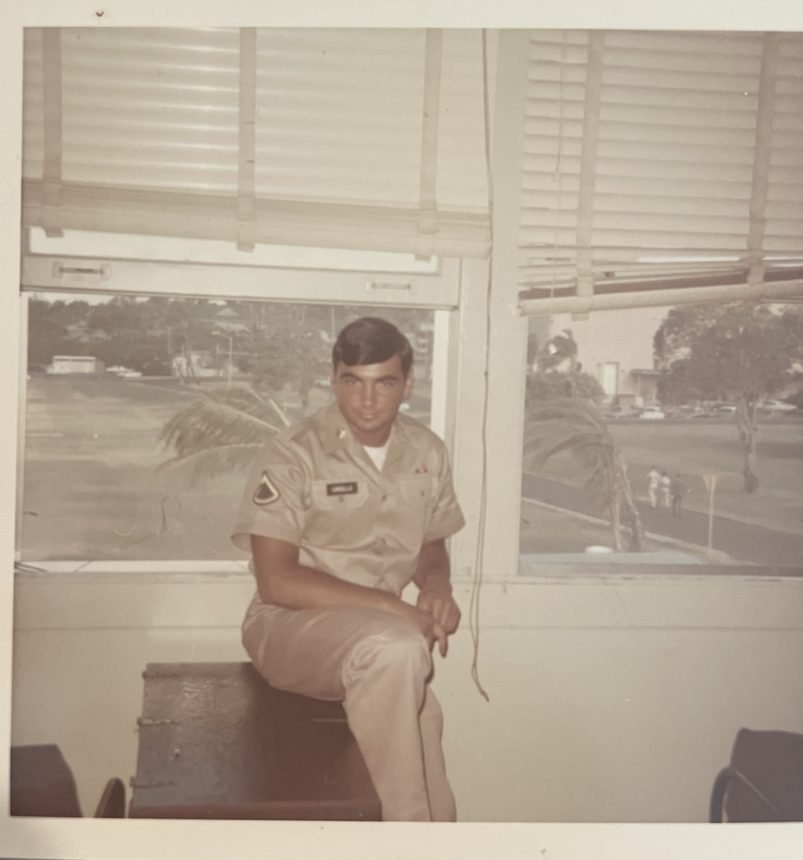 A serviceman in duty khakis seated by a window