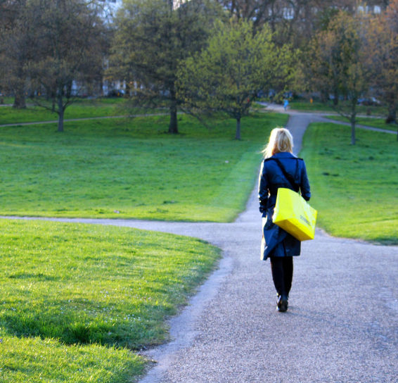 A woman walking down a path carrying a yellow bag.