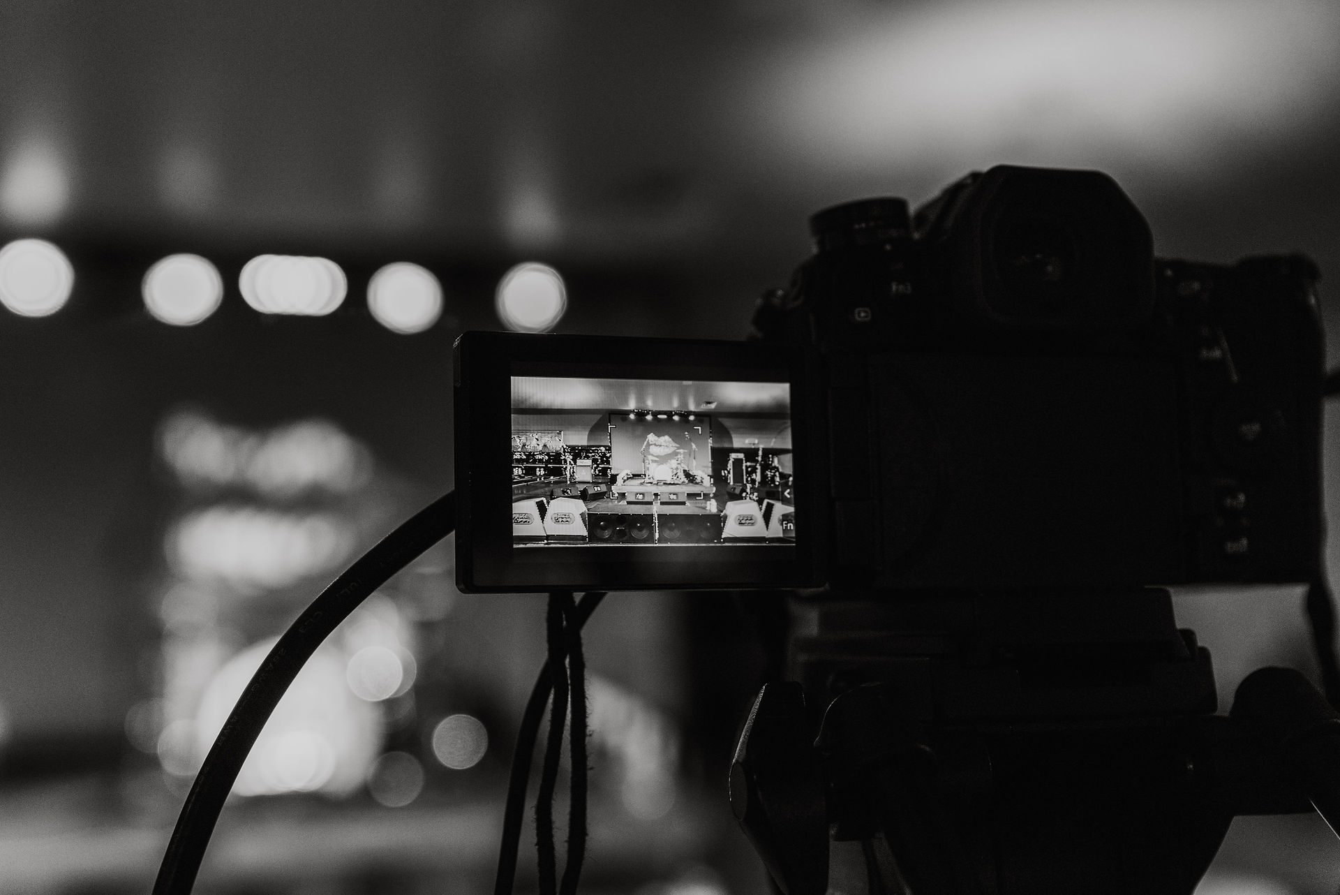 Black and white photo of video camera recording a band performing on stage