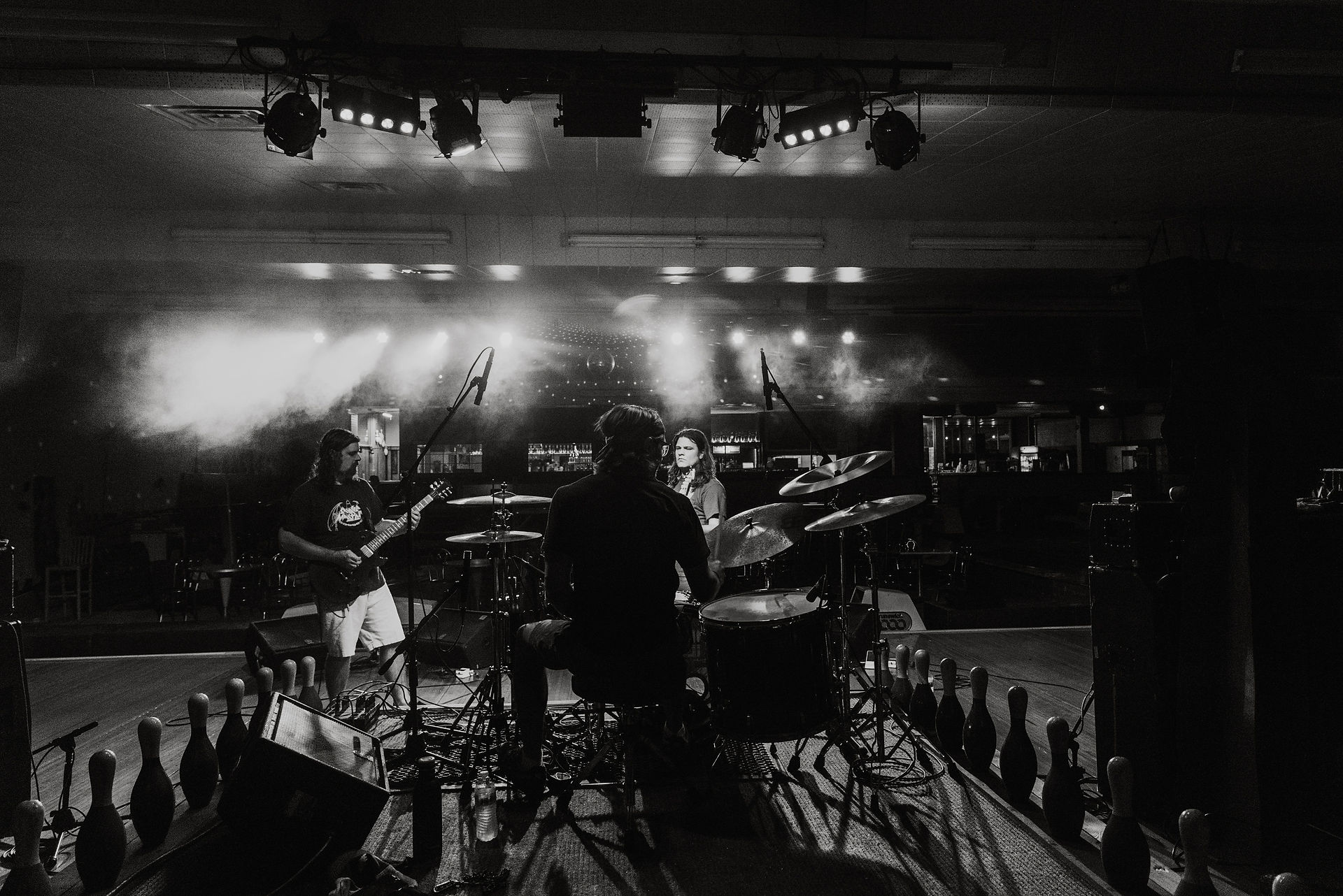 Black and white photo taken from behind the drummer of band performing on stage