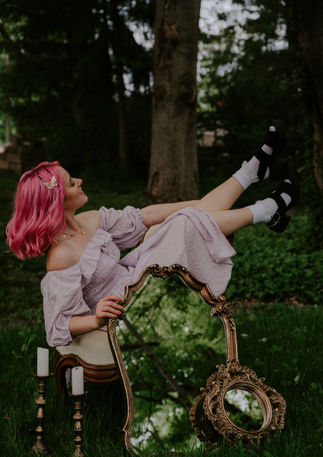 Photograph of a singer-songwriter with brightly colored pink hair in the forest.