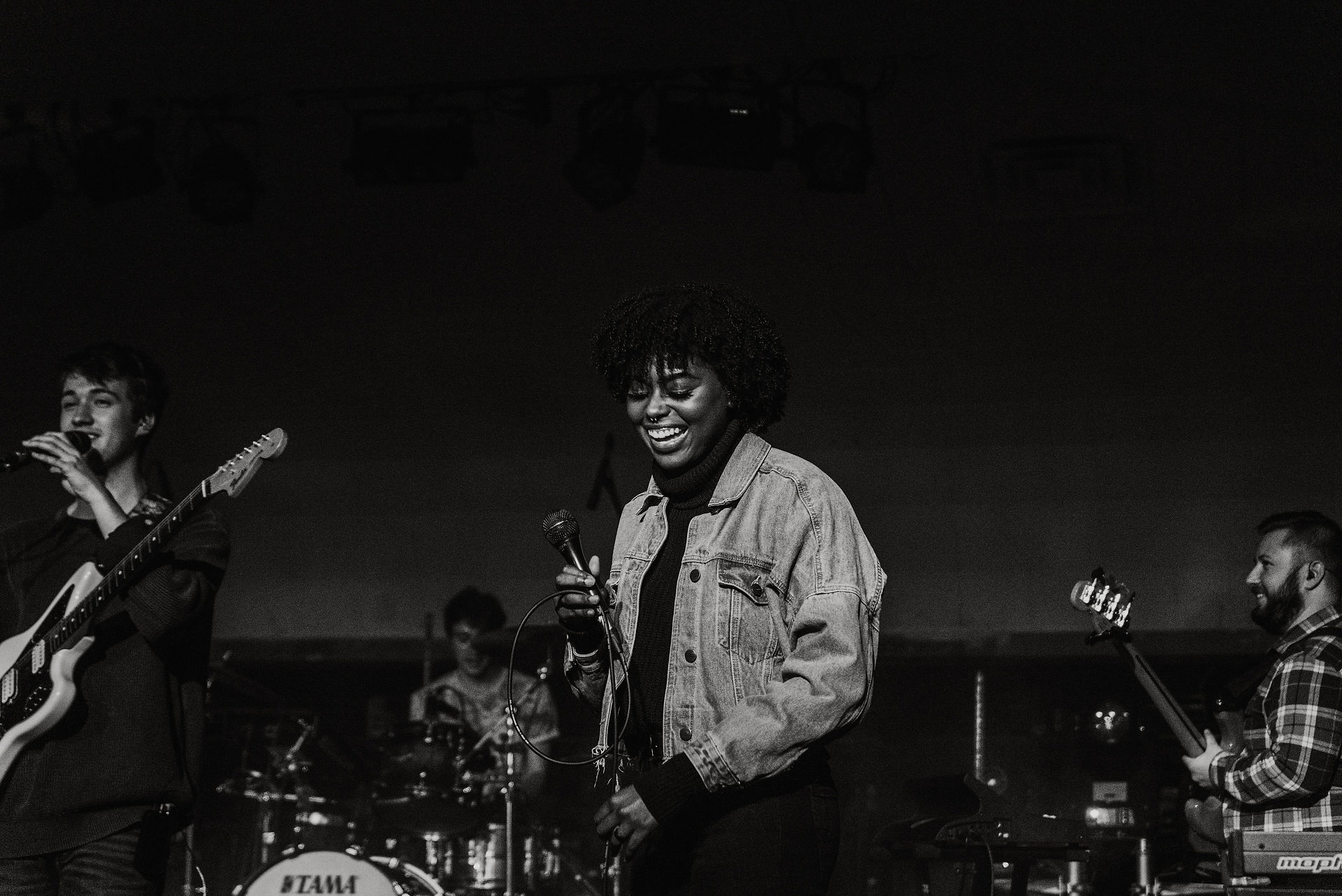 Black and white photo of female vocalist smiling, mid-laugh with her eyes closed holding microphone