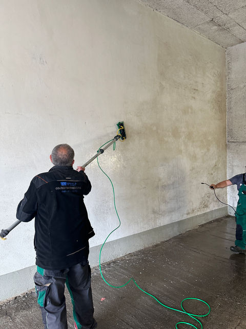 Zwei Arbeiter reinigen mit Hochdruckreinigern eine Wand