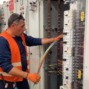 An "Ami & Igal" electrician servicing and wiring an electrical panel in an industrial plant.