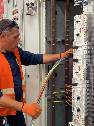 An "Ami & Igal" electrician servicing and wiring an electrical panel in an industrial plant.