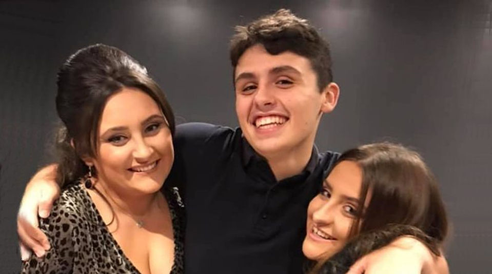 Dylan Price smiling and hugging his two sisters