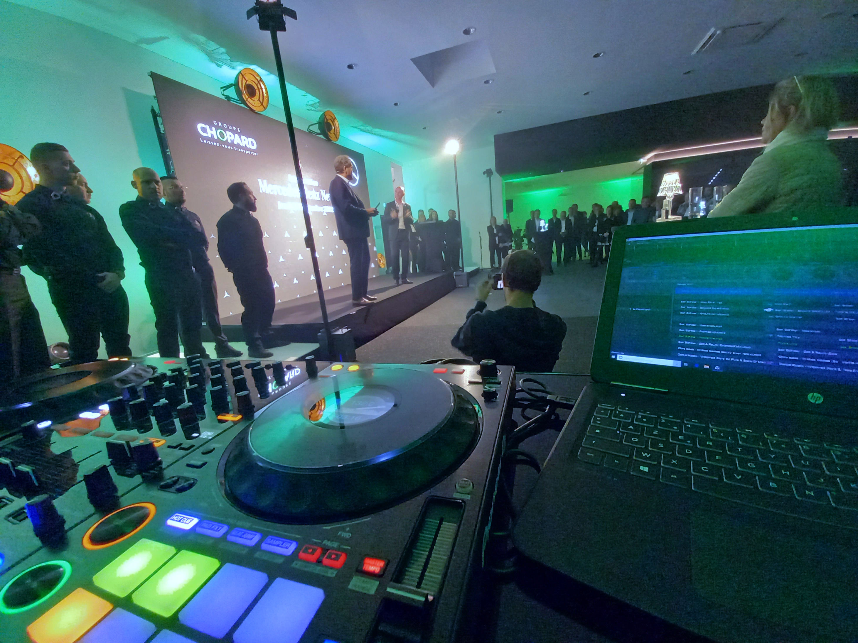 DJ Katanax est devant un publique. Il tient la main d'une personne pour la mettre en avant. Ils sont souriant et adore le moment présent.