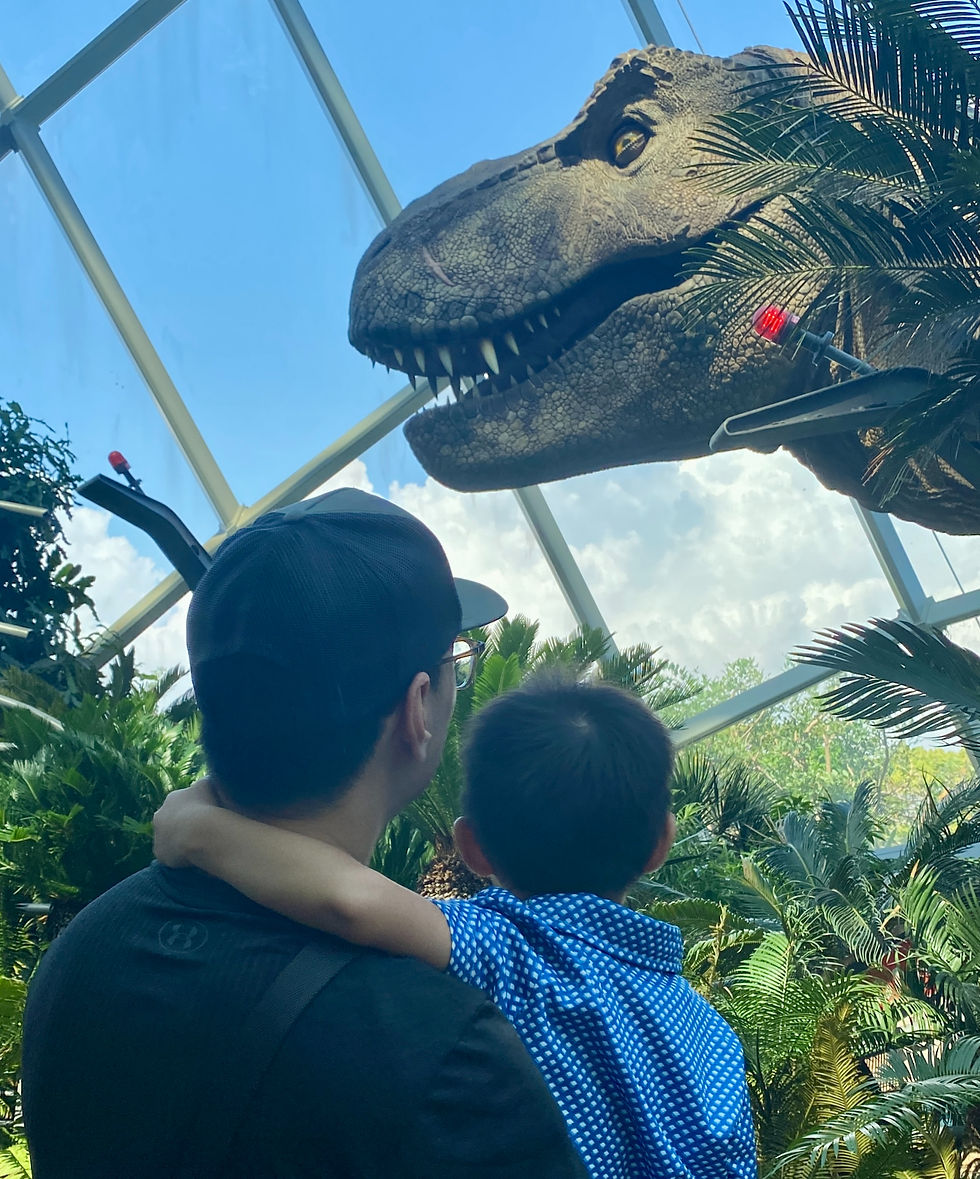 Father holding toddler in front of T. rex display at Jurassic Experience