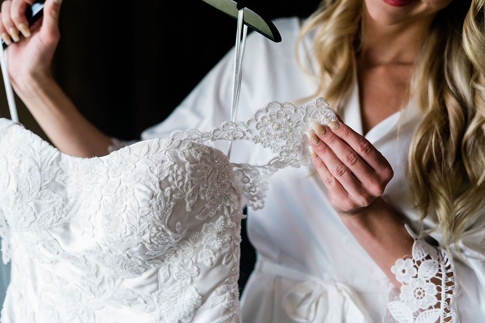 Bride wearing white robe taking lace wedding dress off of hanger