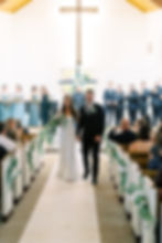 Bride and groom walking in ceremony recessional of church ceremony smiling. Bridesmaids and groomsmen stand behind, clapping with joy
