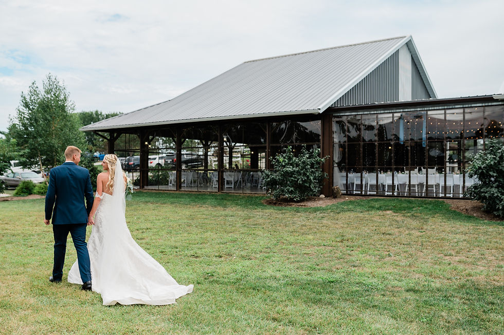 Bride and groom holding hands walking outside of clear walled wedding venue