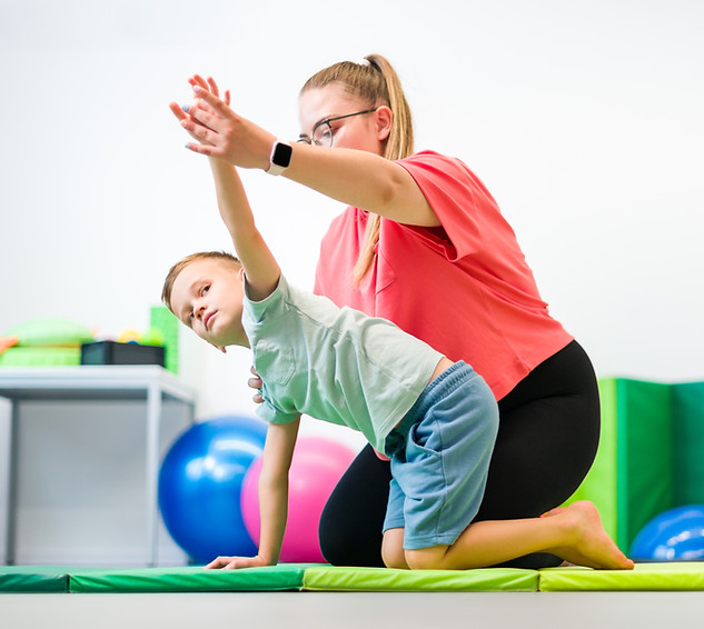Young boy exercising with female physical therapist during therapy session. Child occupati