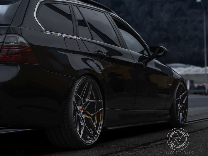 "Im Fokus steht ein beeindruckender BMW 325i Touring, der mit einem atemberaubenden M3 Umbau glänzt. Seine kraftvollen Linien und das charakteristische M3-Design verleihen dem Fahrzeug eine sportliche und zugleich elegante Ausstrahlung. Die tiefdunkle Lackierung betont nicht nur die Individualität, sondern verleiht dem Wagen auch eine luxuriöse Note. Die maßgeschneiderten M3-Stoßstangen, Seitenschweller und der markante Frontgrill lassen erkennen, dass hier Performance im Mittelpunkt steht. Die Japan Racing Wheels und die gekonnt abgesenkte Fahrwerkshöhe unterstreichen den dynamischen Charakter des Fahrzeugs, während die präzise gestalteten Auspuffendrohre einen Hauch von Rennsport vermitteln. Dieses Bild offenbart die gelungene Symbiose aus Luxus und Performance im Rahmen des BMW 325i Touring M3 Umbaus."