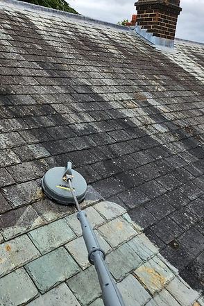 A roof being cleaned in Enfield the cleaning tool rests on the roof showing the part that is clean and the rest which is dirty