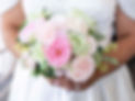 Close up of a beautiful bouquet of flowers featuring pale pinj, peach and green flowers helf by a bride.
