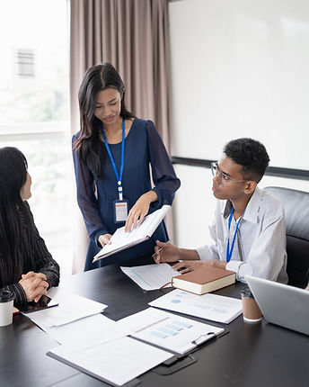 A lady in a blue dress wearing a lanyard holds a notebook of stats whilst a colleague sits nearby