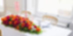 Deep red, pink and orange flowers placed on a well dressed table which has candles, plates & glasses.