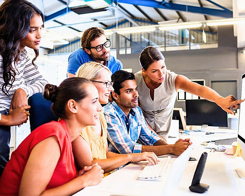 A group of adults huddled around a computer as a lady points at the screen