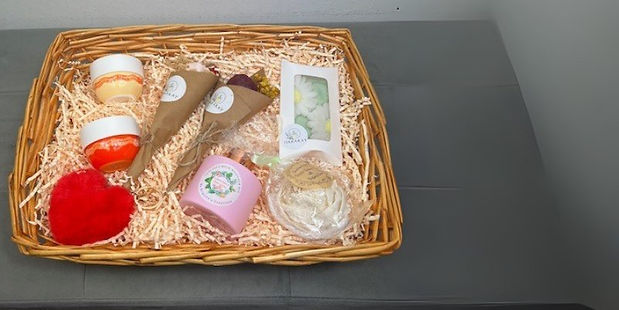 A rectangular brown wicker gift basket with mii bouquets of flowers, creams and candles inside