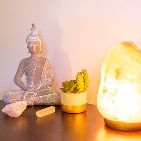 A sideboard with a Budha, a plant, a salt lamp and a few crystals
