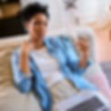 A lady wearing white t--shirt and denim shirt sits on her sofa and fans herself with paper