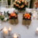 Brown gift bags of deep red and orange flowers placed on a table with a white tablecloth and a big vase of matching flowers