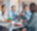 2 smartly dressed men, and 2 smartly dressed women talk around a table with a laptop open